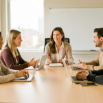 Une manager échange avec une équipe diverse autour d’une table dans un bureau lumineux et professionnel.